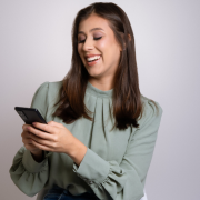 Mujer sonriente revisando su teléfono móvil, representando entusiasmo y satisfacción en la búsqueda de empleo o en el uso de herramientas digitales para su crecimiento profesional.