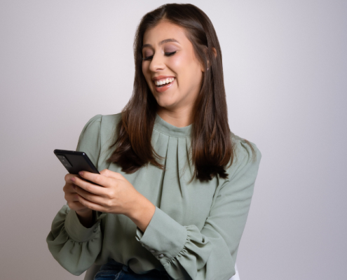 Mujer sonriente revisando su teléfono móvil, representando entusiasmo y satisfacción en la búsqueda de empleo o en el uso de herramientas digitales para su crecimiento profesional.